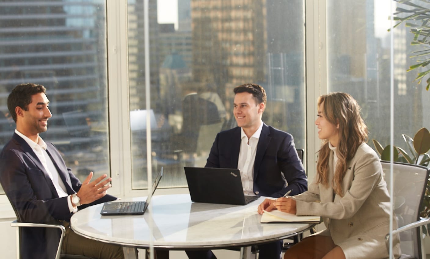 People talking at a small table in front of big windows